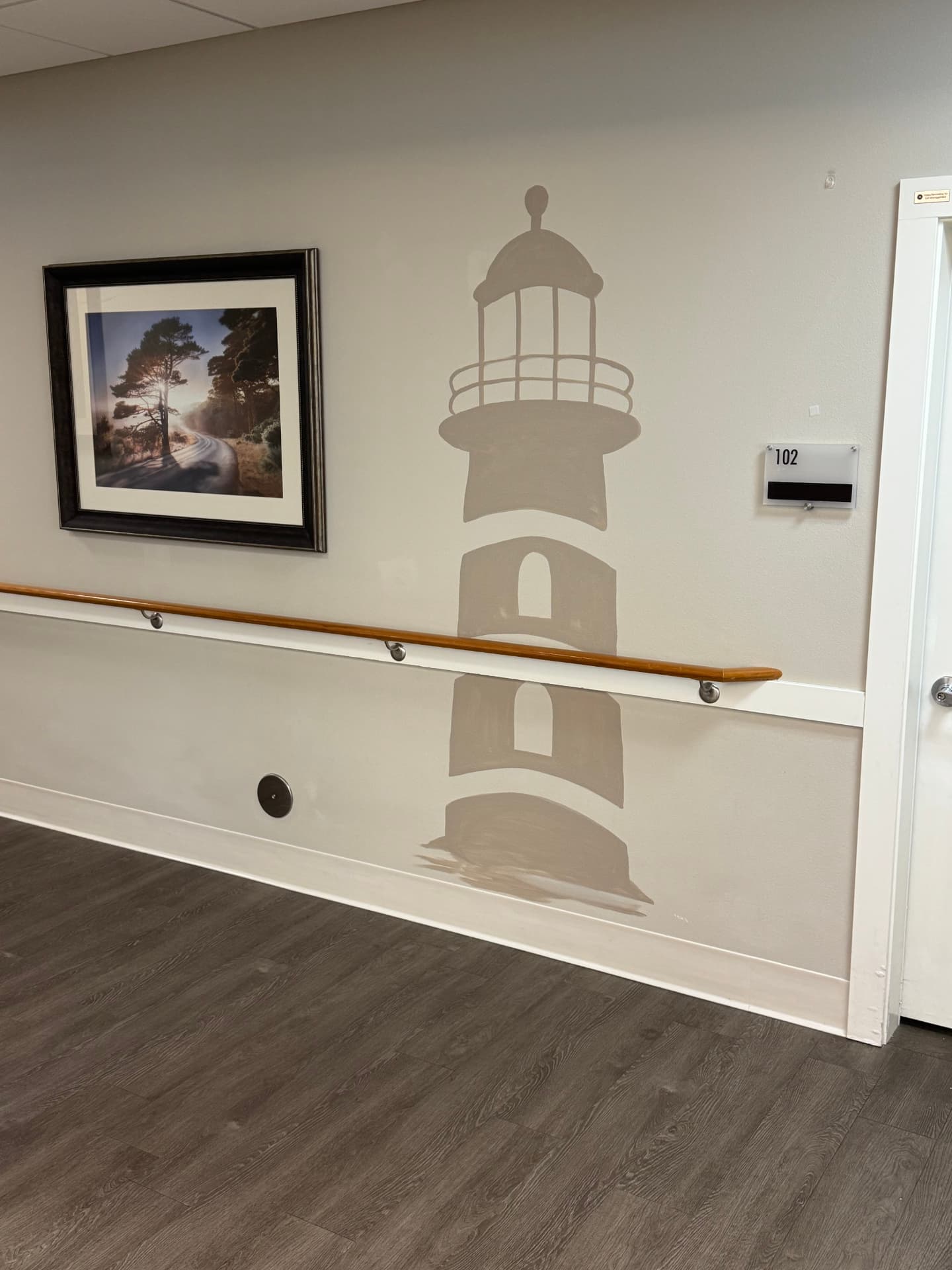 Hallway at Lighthouse Memory Care with a painted lighthouse mural, a wooden handrail and a resident room door