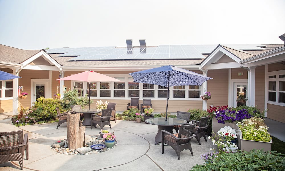 Courtyard seating with wicker furniture under pink and blue umbrellas at Lighthouse Memory Care